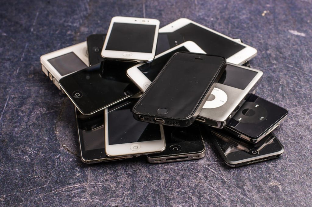 Stack of assorted aged cellphones with black screens and portable music players on gray background